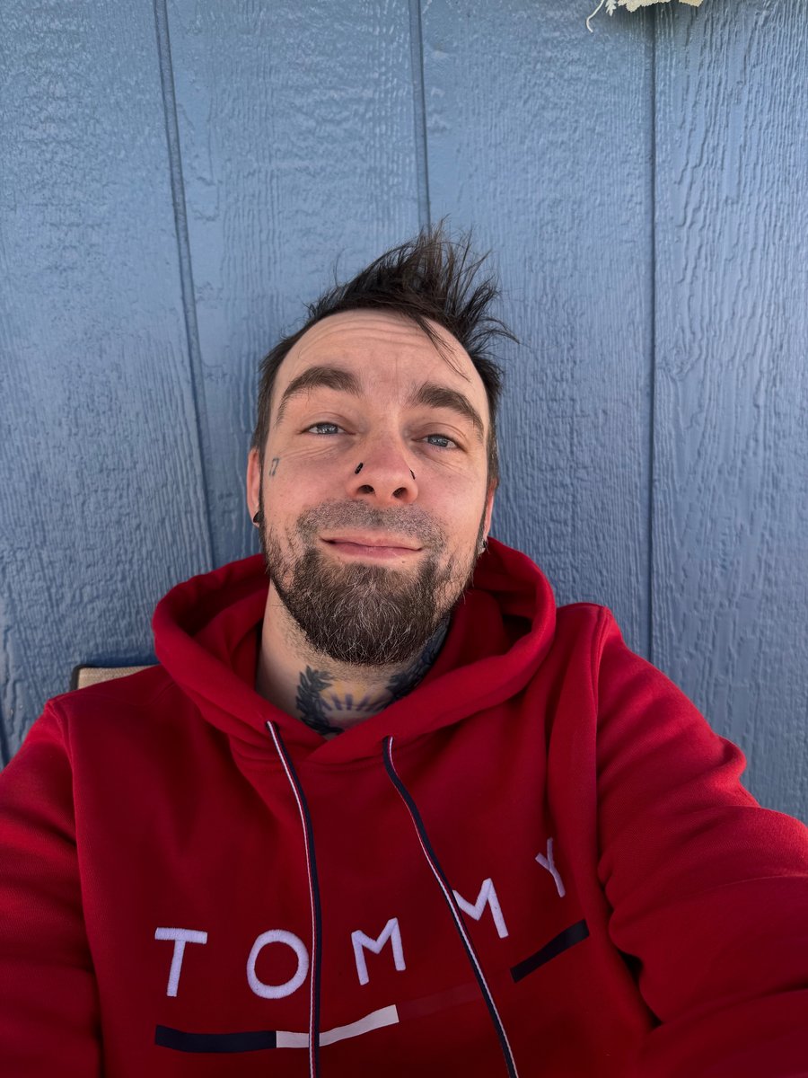 Danny Thomas smiling in a red hoodie against a blue wall
